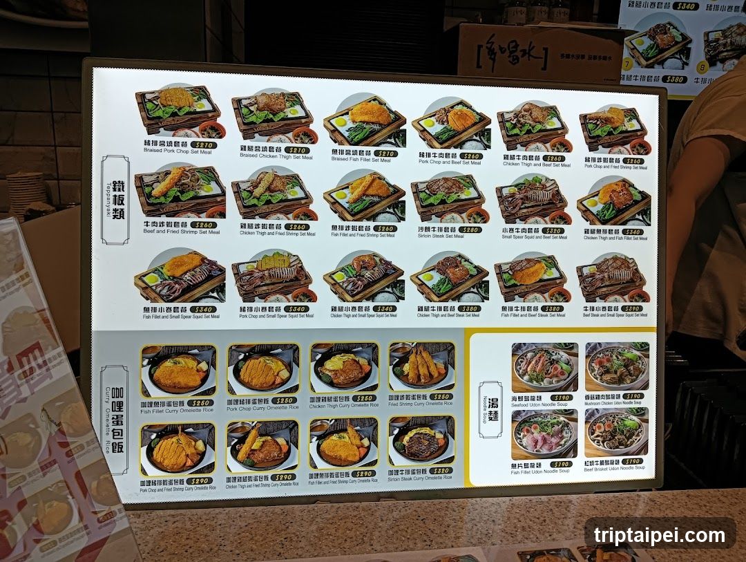 A digital menu board displaying various bento box options with prices in HKD, organized into categories like 'Bento Box' and 'Omelet Rice Bowl'. The menu includes items such as 'Beef and Fried Egg Set Meal', 'Chicken High and Small Sweet Set Meal', and 'Pork Chop and Beef Stew Set Meal'. Prices range from 21 to 39 HKD.