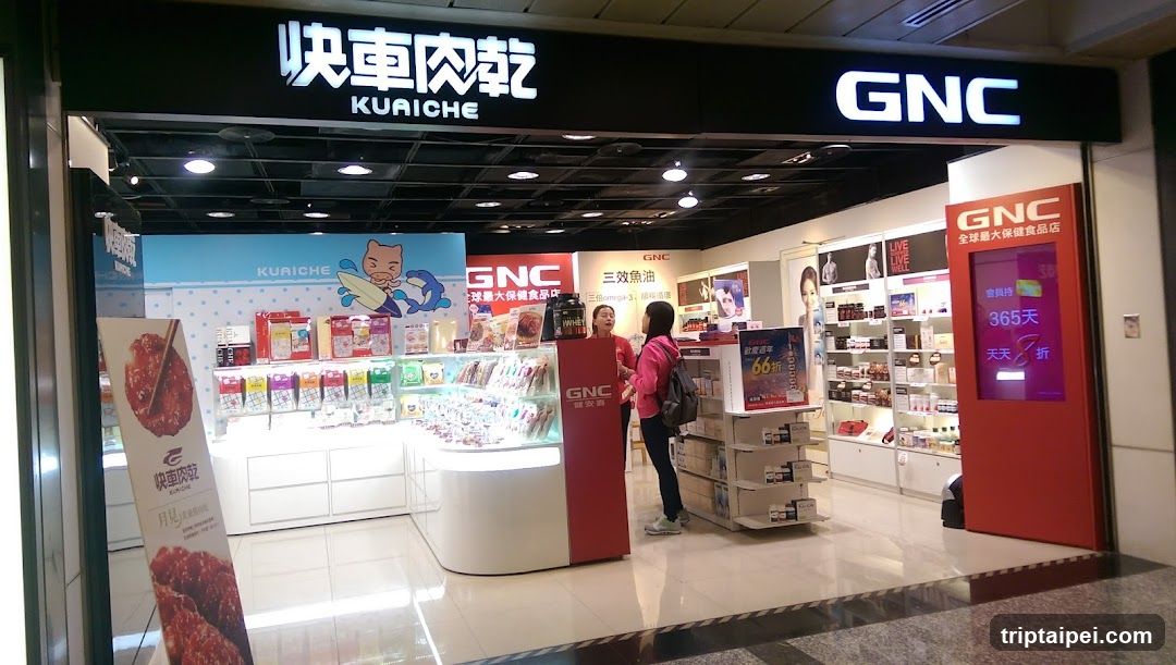 The image shows the exterior entrance of a store with two prominent signs: 'KuaiChe' (快車肉乾) on the left and 'GNC' on the right. The interior is visible, featuring shelves stocked with various products, including snacks and health supplements. Two individuals are standing near the center, possibly browsing or interacting with staff. A large poster advertising 'KuaiChe' is placed outside the store.