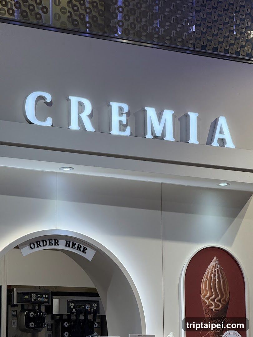 The image shows the exterior of a Creemia store, featuring illuminated signage with the brand name 'CREEMIA' prominently displayed above an arched entrance labeled 'ORDER HERE'. Inside, soft-serve ice cream machines are visible, and to the right, there is a poster showcasing a swirled ice cream cone.
