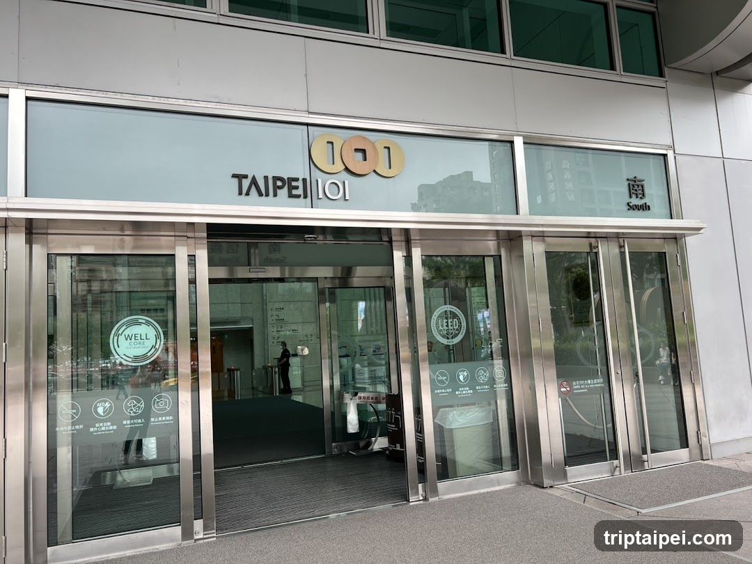 Photo of the physical exterior entrance storefront facade of Taipei 101, showing glass doors with signage reading 'TAIPEI 101' and 'South', along with LEED certification logos on the door panels.