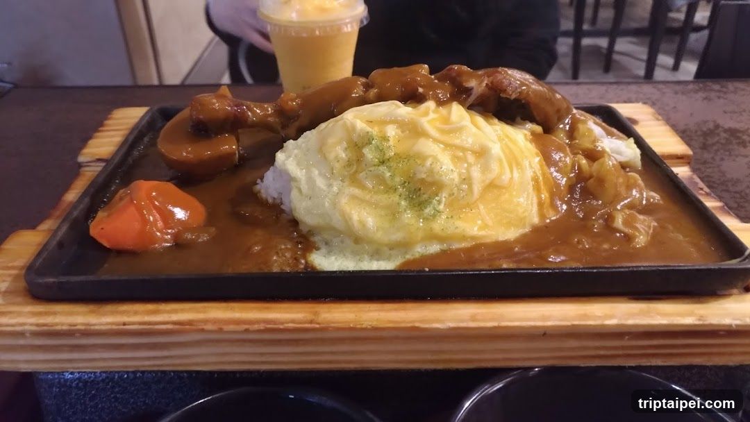 A close-up of a Japanese curry rice dish served on a black rectangular plate, placed on a wooden tray. The dish includes white rice topped with a large mound of creamy egg custard (tamagoyaki), covered in rich brown curry sauce. Visible ingredients include chunks of meat (possibly pork or chicken), mushrooms, carrots, and cabbage. In the background, slightly out of focus, is a person holding a yellow beverage cup.