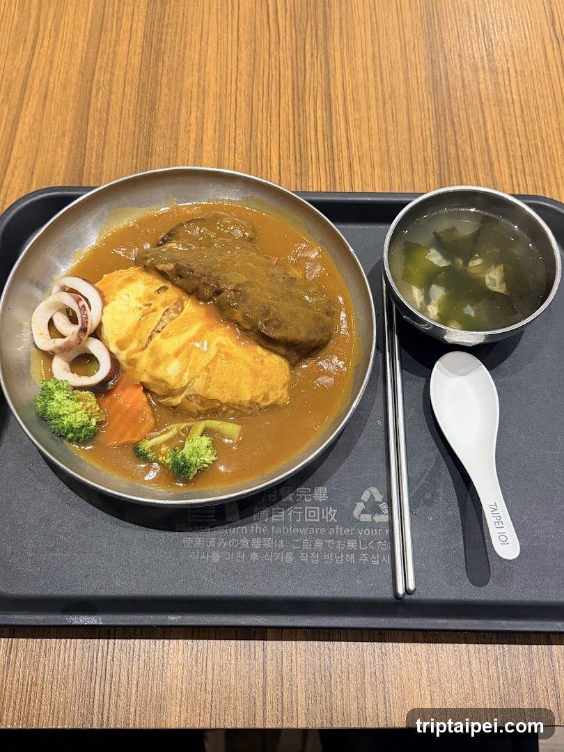A tray with a bowl of curry rice topped with omelette and beef, accompanied by seaweed soup and chopsticks.
