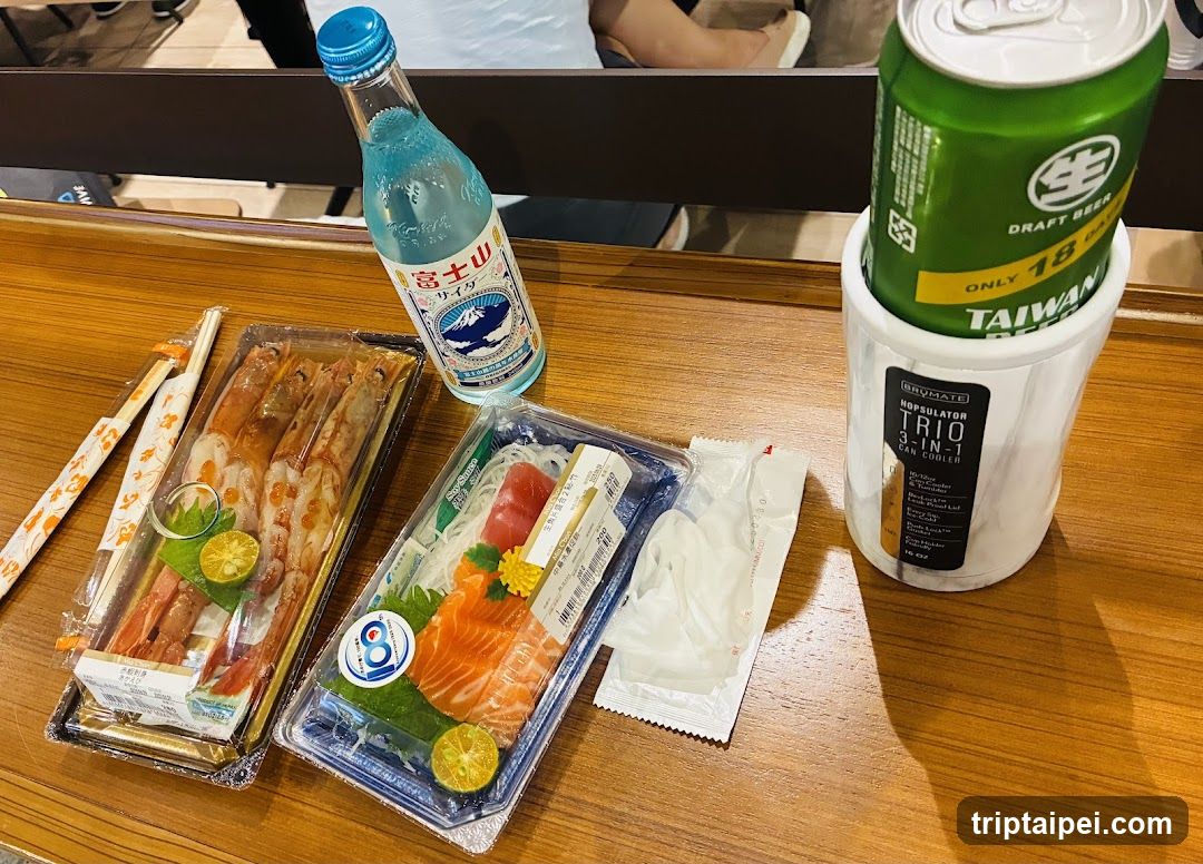 A table display featuring a bottle of Izakaya water, a can of Taiwan beer in an insulated cup, two trays of sushi (one with shrimp, one with salmon sashimi), and chopsticks wrapped in paper.