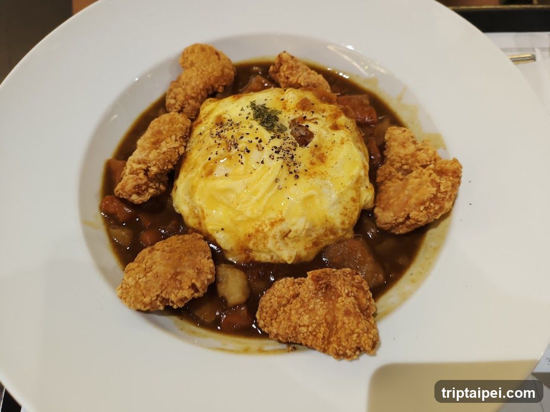 A plate of crispy fried chicken pieces arranged around a mound of yellow rice, all covered in a rich brown curry sauce.
