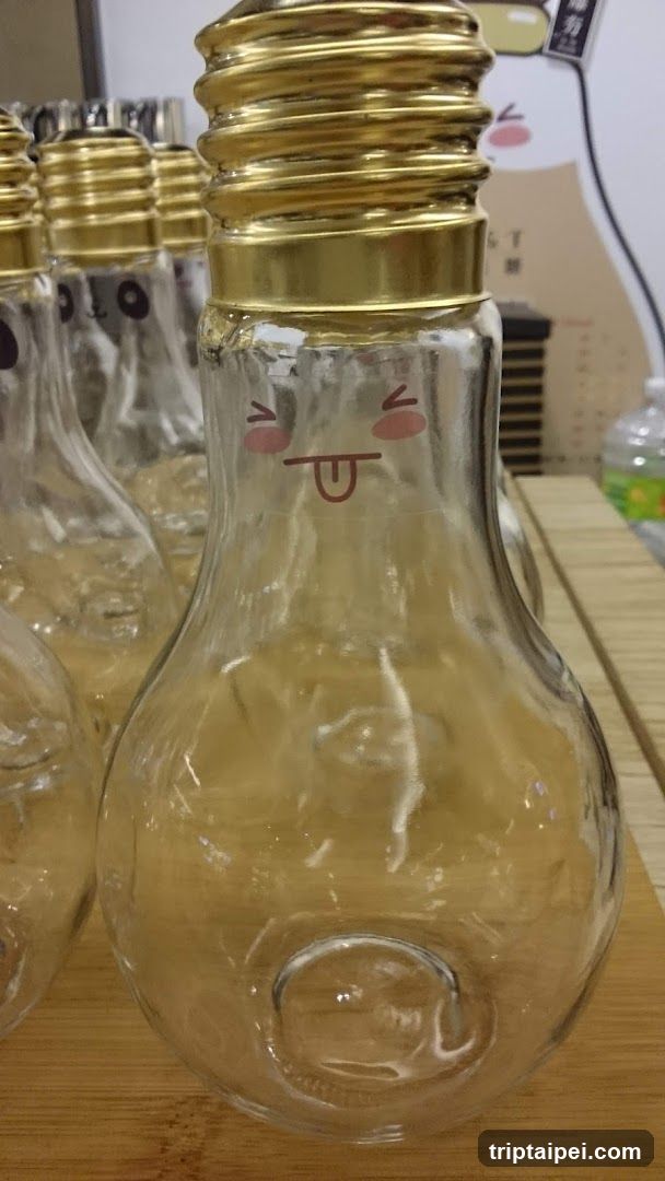Close-up of clear glass bottles shaped like light bulbs with gold screw caps and a cute face printed on the glass.