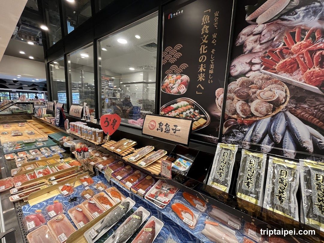 A well-lit seafood section in a modern store, featuring fresh fish and shellfish on display counters. Promotional posters advertise Japanese culinary culture and products like 'Umi no Kuni' (Land of the Sea). Shelves are stocked with packaged seafood items.