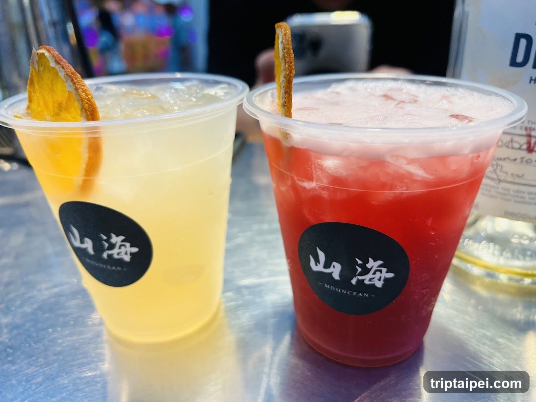 A close-up of two plastic cups filled with colorful beverages, one yellow and one red, both garnished with orange slices. The cups feature a black circular logo with Chinese characters '山海' (Shanhai) and the English word 'MOUNCAN'. The background is slightly blurred, showing hints of a bar or restaurant setting.
